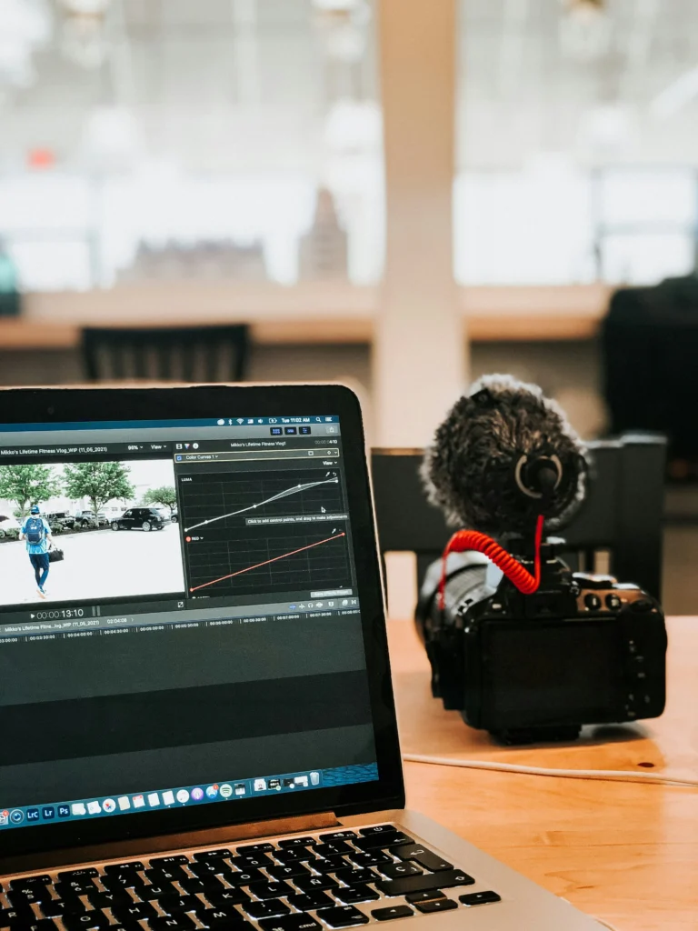 A camera and a laptop displaying video editing software on a wooden desk