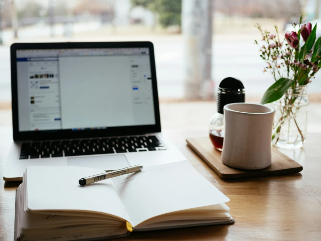 Computer on desk with notepad, pen, and coffee cup